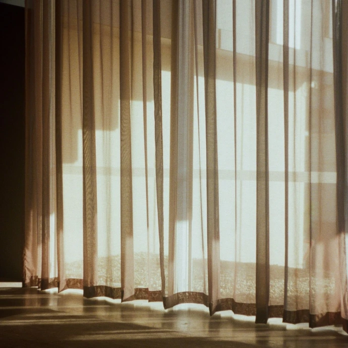 a room with a bed and a window with sheer curtains